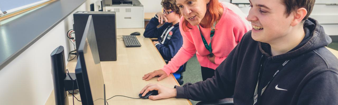 A tutor working a young man on a computer 